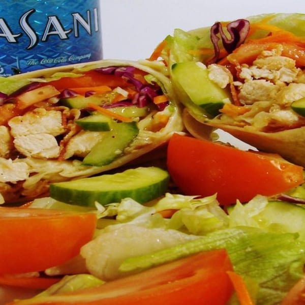 Two chicken wraps filled with lettuce, cucumber, carrots, and red cabbage, with a Dasani bottle.