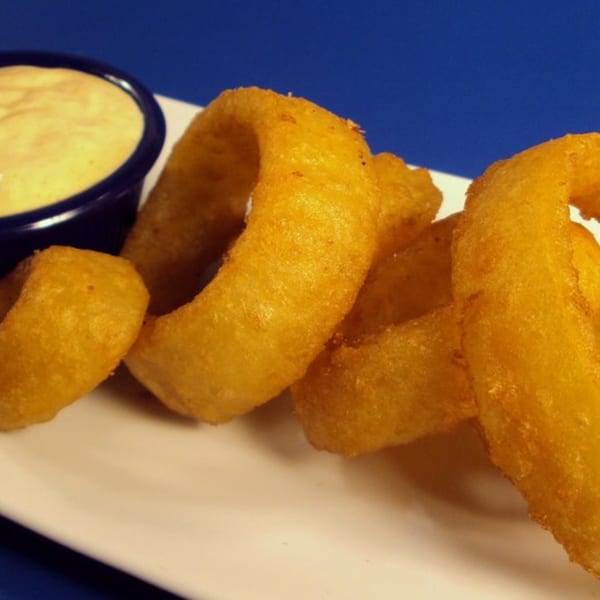 Golden-brown onion rings on a white plate with a side of creamy dipping sauce.