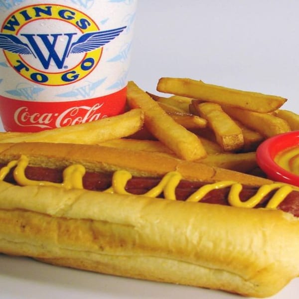 A hot dog with mustard, french fries, and a Wings to Go Coca-Cola cup.