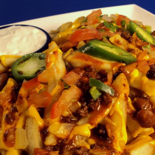 Chili cheese fries with jalapeños and diced tomatoes, served with a side of sour cream.